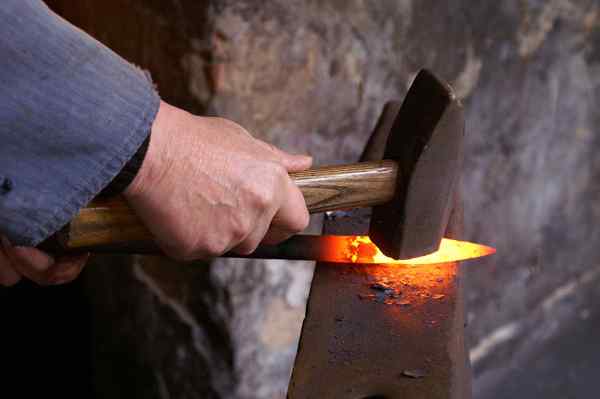 Taller De Forja. Producción Manual De Herrería. Manos De Herrero Con Golpe  De Martillo En Metal Caliente Brillante, En El Yunque, El Proceso De Forja.  El Herrero Fabrica Productos De Hierro Para